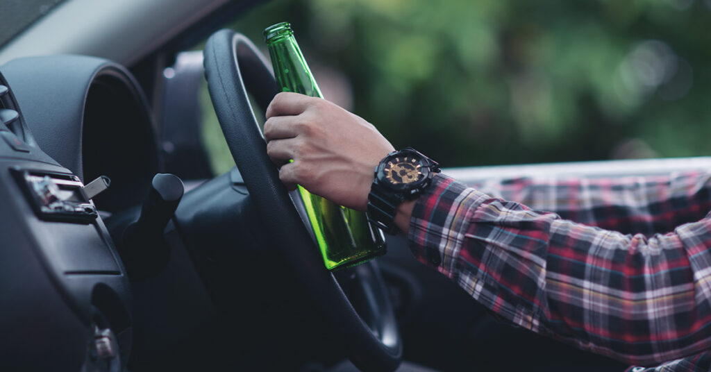 Close-up of a person holding a beer bottle while driving.
