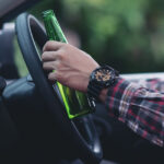 Close-up of a person holding a beer bottle while driving.