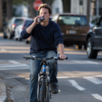 Man riding a bicycle while drinking alcohol on a city street.