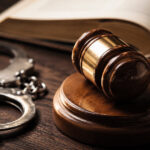 Judge’s gavel, handcuffs, and an open law book on a wooden table