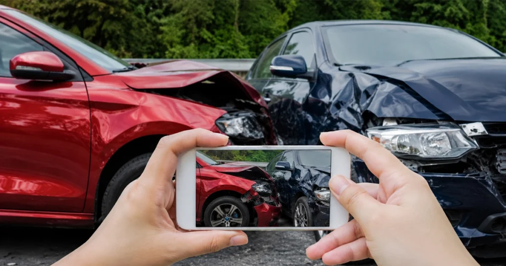 Hands photographing two damaged cars after a collision.
