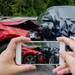 Hands photographing two damaged cars after a collision.