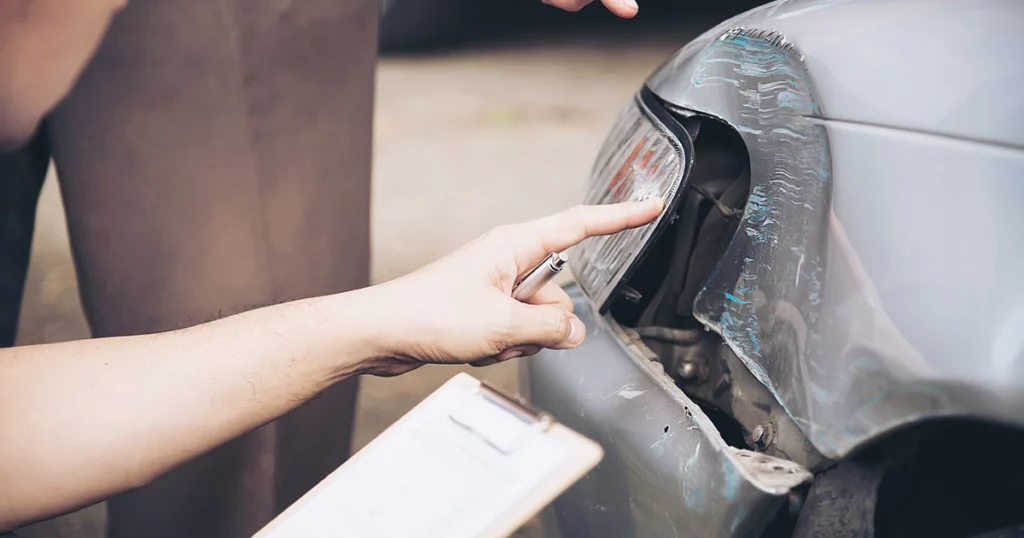 Insurance adjuster inspecting a car’s damaged taillight and bumper.