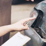 Insurance adjuster inspecting a car’s damaged taillight and bumper.