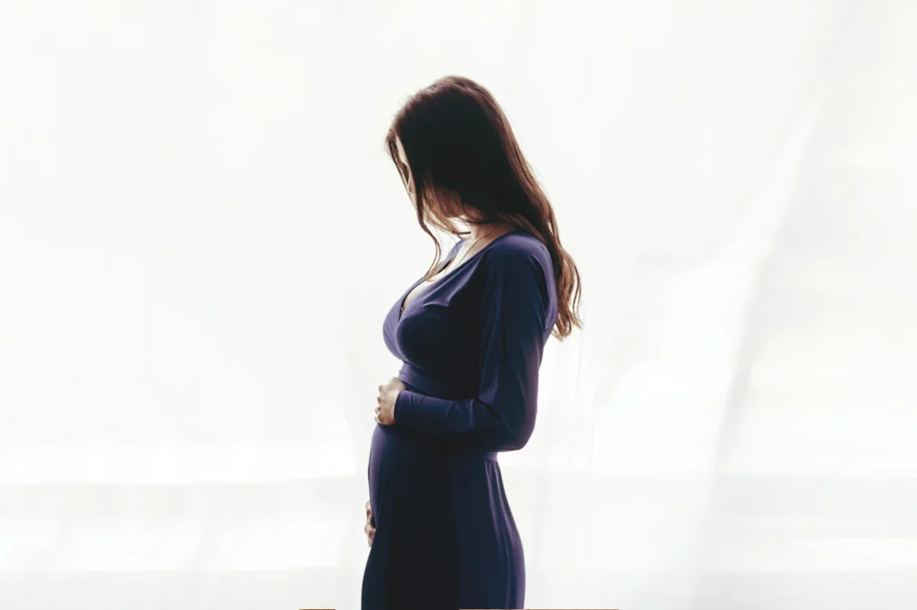 Pregnant woman in a dark dress cradling her belly.