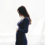 Pregnant woman in a dark dress cradling her belly.