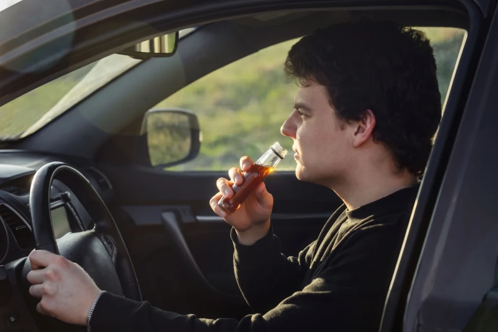 Side view profile of a man drinking alcohol from a small glass bottle while driving