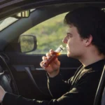 Side view profile of a man drinking alcohol from a small glass bottle while driving