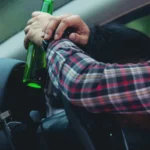 Drunk driver leaning on the steering wheel holding a beer bottle.